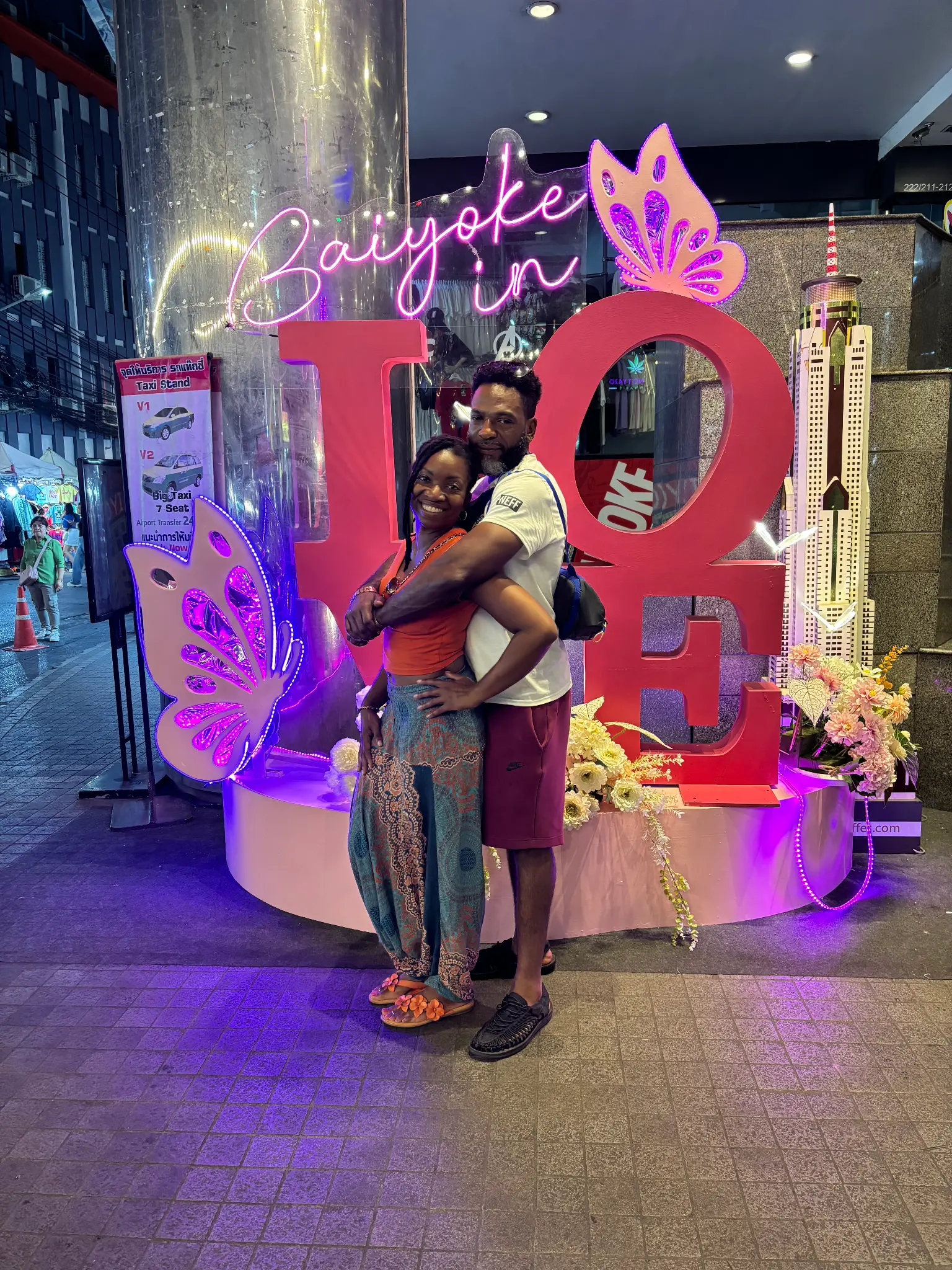 Zen & Cody embracing in front of a LOVE sign in Bangkok